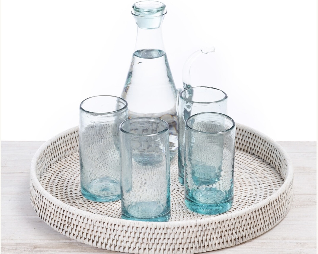 Rattan round tray with sea-glass blue tumblers styled on a pale wood surface in a coastal interior