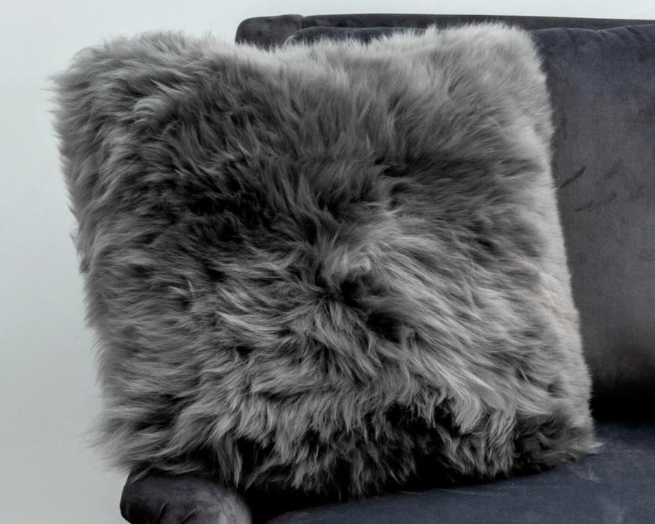 Grey sheepskin cushion styled with orange cushions and a navy sofa