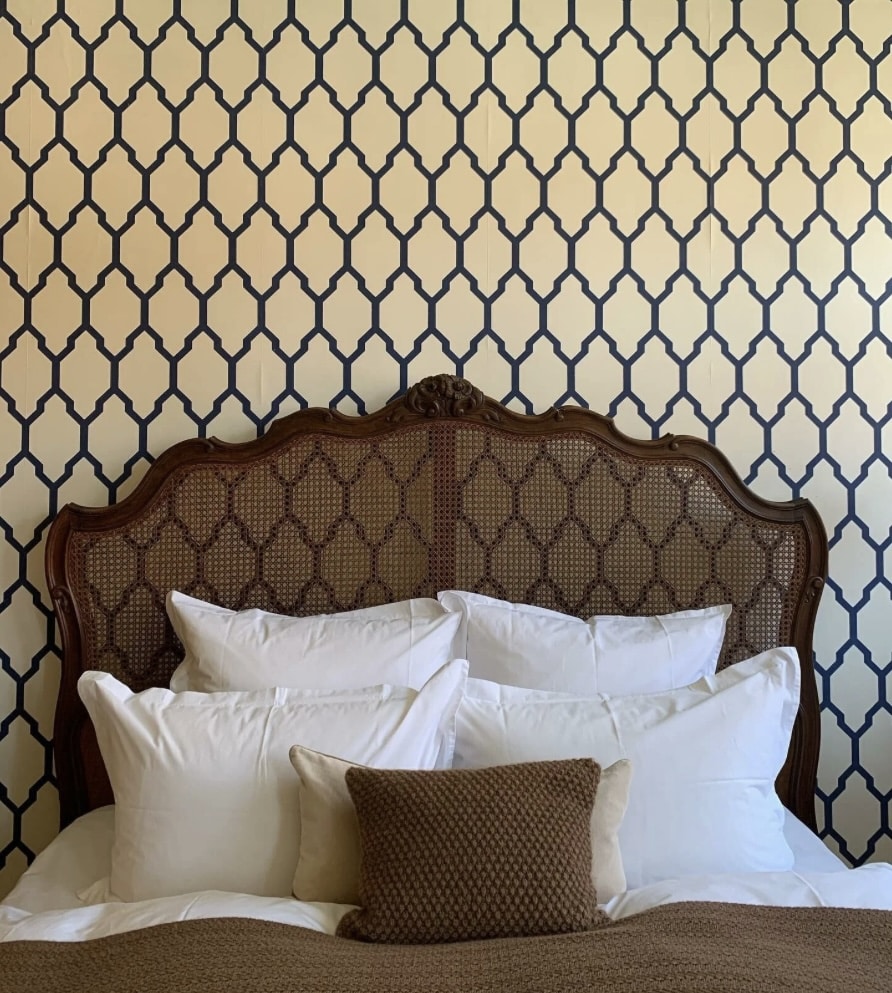 Bedroom wallpaper ideas: blue-and-cream Tessella trellis wallpaper feature wall behind the bed with cane headboard and layered white bedding.