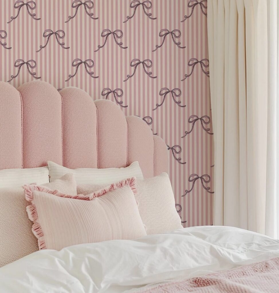 Pink bow wallpaper with blush striped wallpaper pattern behind a scalloped pink headboard and white bedding – cute bedroom wallpaper ideas.