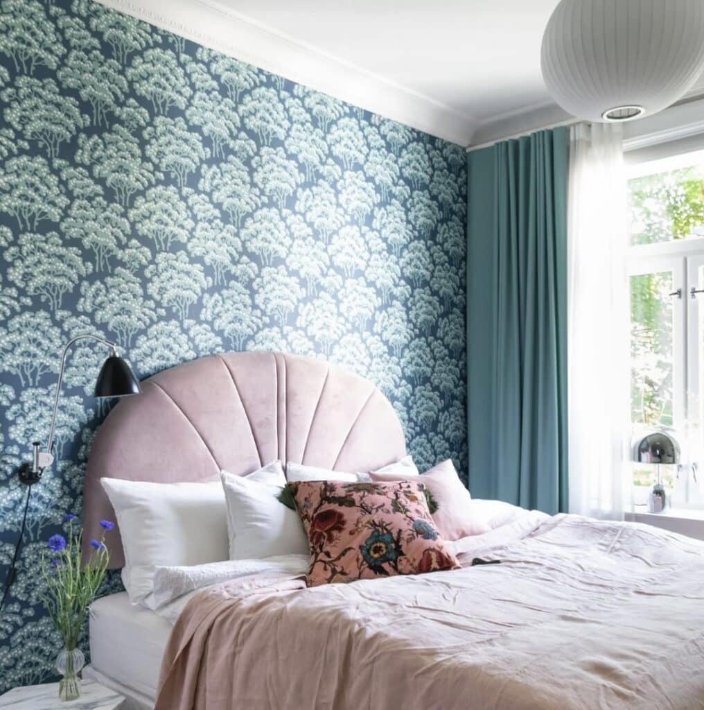 Hornbeam Wallpaper by Farrow & Ball on a feature wall behind the bed, teal-green botanical pattern with blush headboard, soft pink bedding and teal curtains