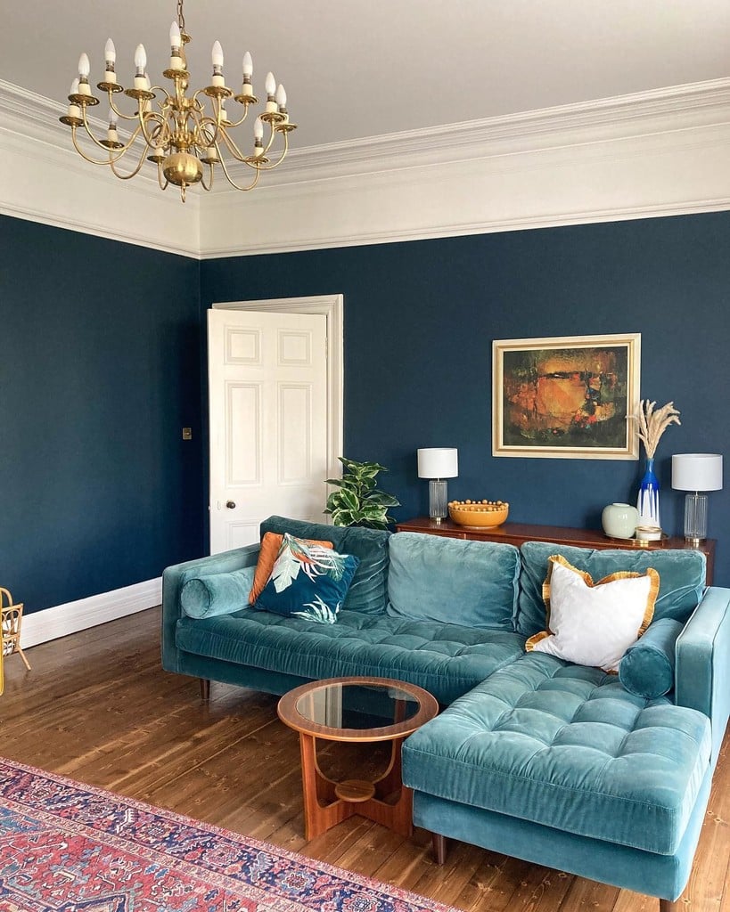 Teal velvet corner sofa with an orange tropical print cushion against walls painted in Farrow & Ball Hague Blue