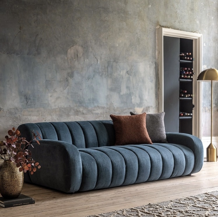 Blue fabric sofa styled with burnt orange velvet cushions for a warm contrast in a modern living room.