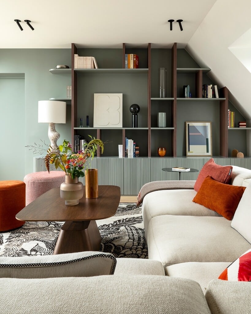 Burnt orange cushions on a cream sofa against shelving painted in Farrow & Ball Pigeon, with an orange pouffe