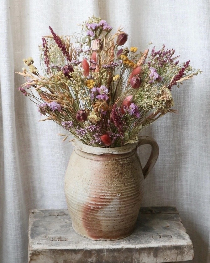 Dried flower bouquet in a rustic stoneware jug on a vintage wooden stool