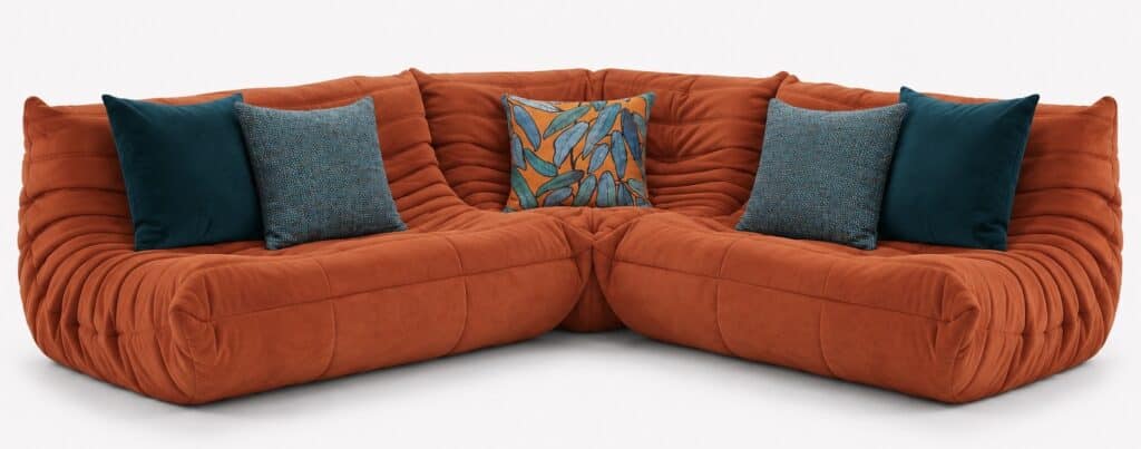 Ligne Roset Togo orange corner sofa styled with teal velvet, textured teal and orange botanical cushions in a modern retro living room setting.