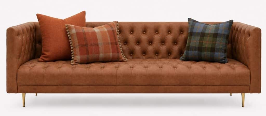 Cognac leather Chesterfield-style sofa styled with burnt orange and tartan tweed cushions for a warm heritage-inspired living room look.