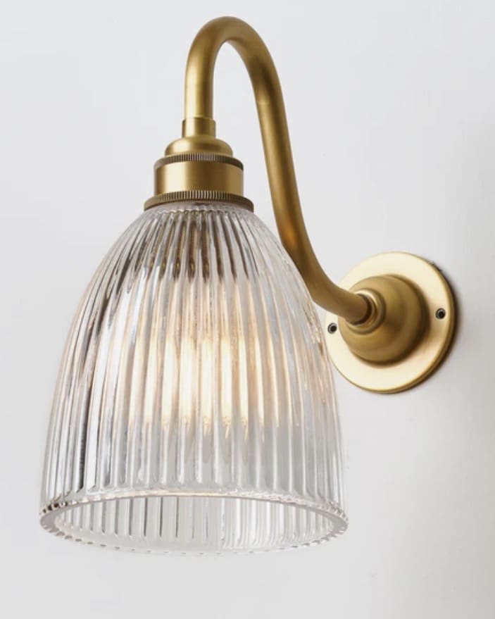 Prismatic glass wall light with swan arm in satin brass adds vintage charm to a neutral bathroom