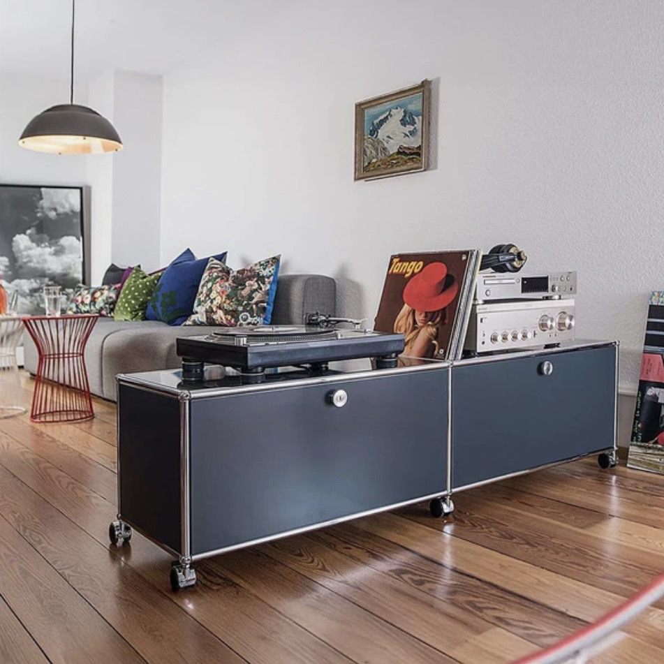 USM Haller Media Unit M61 in Steel Blue used as a low room divider behind a sofa, a sleek living room storage idea for zoning open-plan spaces and hiding clutter.