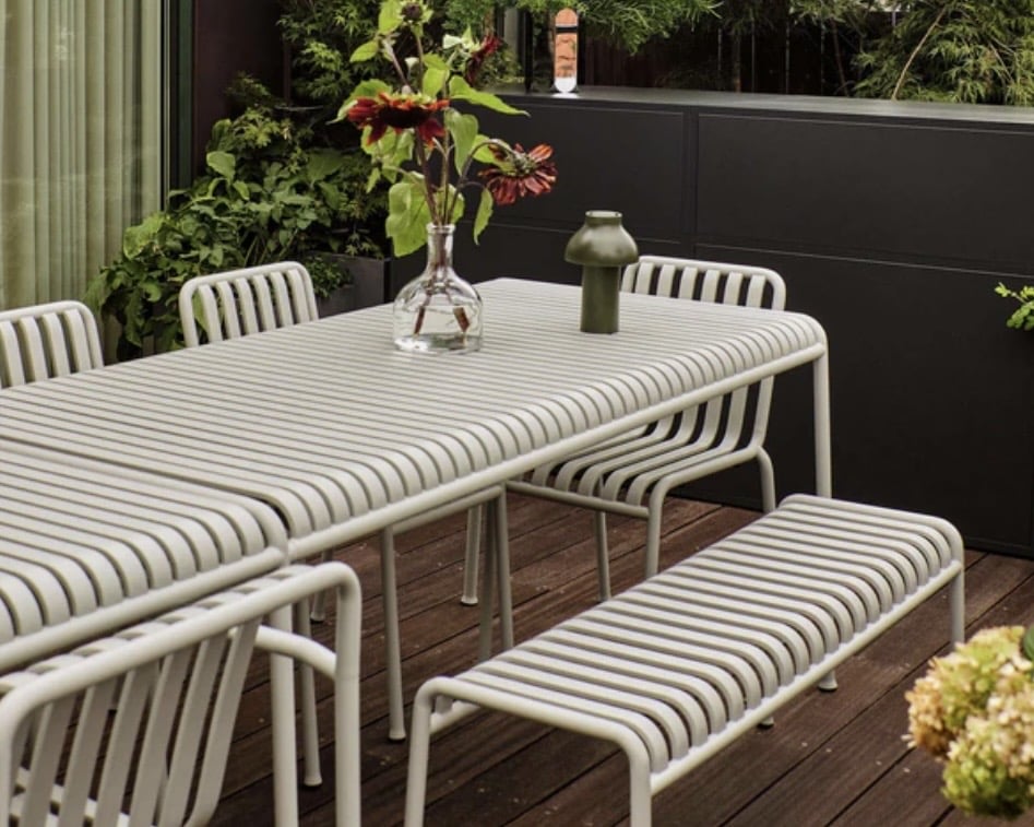 Light-toned slatted metal outdoor dining table in a planted courtyard, ideal for small courtyard garden ideas