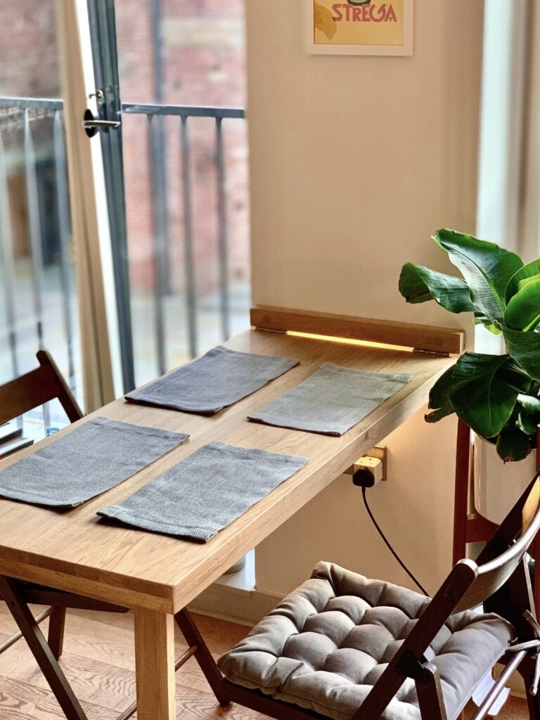 Small dining room ideas featuring a wall-mounted fold-down oak dining table styled for two beside large windows in a compact flat.