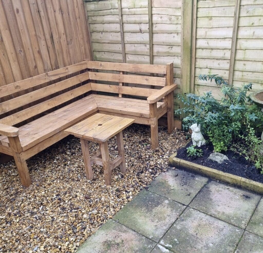 Small garden corner garden sofa bench in timber with a tiny square table beside a paved walkway.