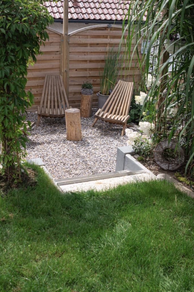 Small garden ideas UK: low maintenance gravel garden with wooden sun lounger, ornamental grasses and hydrangeas against timber panel fencing