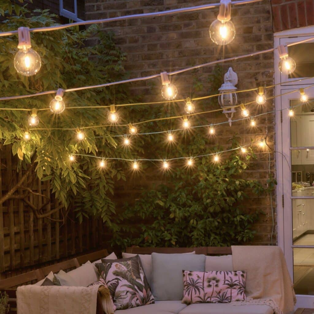 Small garden ideas: warm festoon string lights over a cosy patio seating area, creating a soft evening glow in a compact garden.