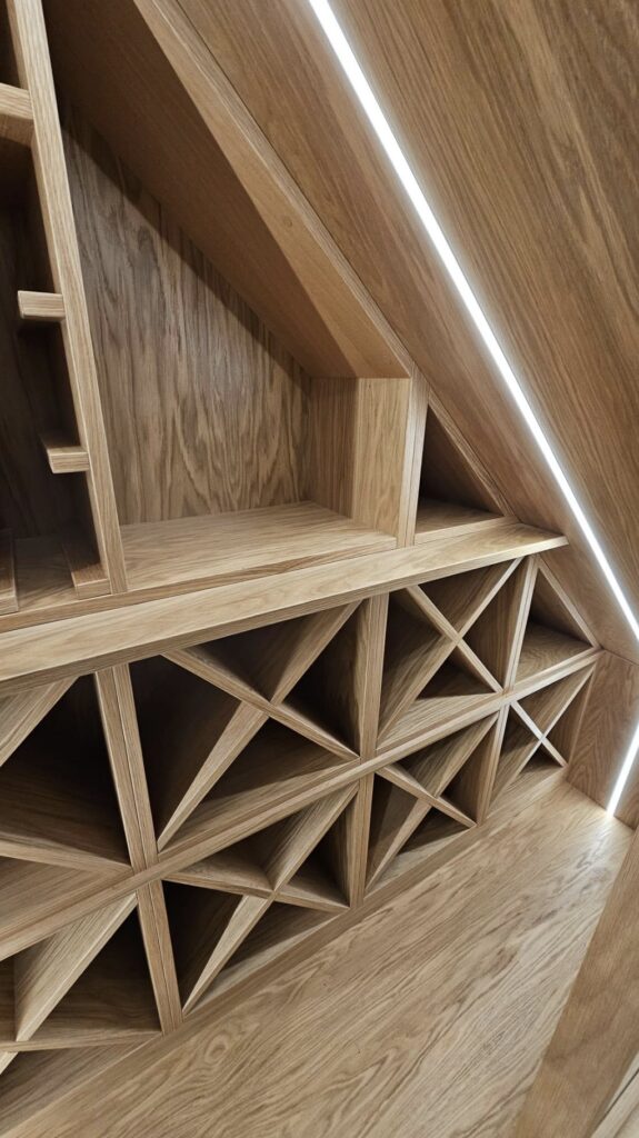 Close-up of a bespoke pale oak under-stairs wine rack with geometric cubbies and integrated LED strip lighting.