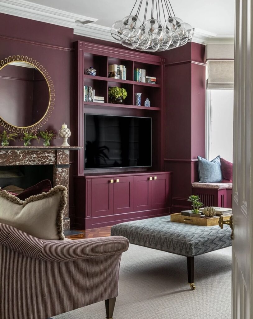 Living room storage ideas featuring built-in TV wall cabinetry painted in Brinjal by Farrow & Ball with concealed cupboards and open shelving, design by Ottadesign.