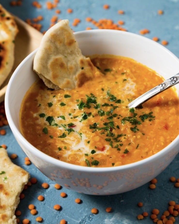 Spicy carrot and lentil soup in a bowl with a swirl of yoghurt and fresh herbs – a warming, cosy dinner for chilly evenings.