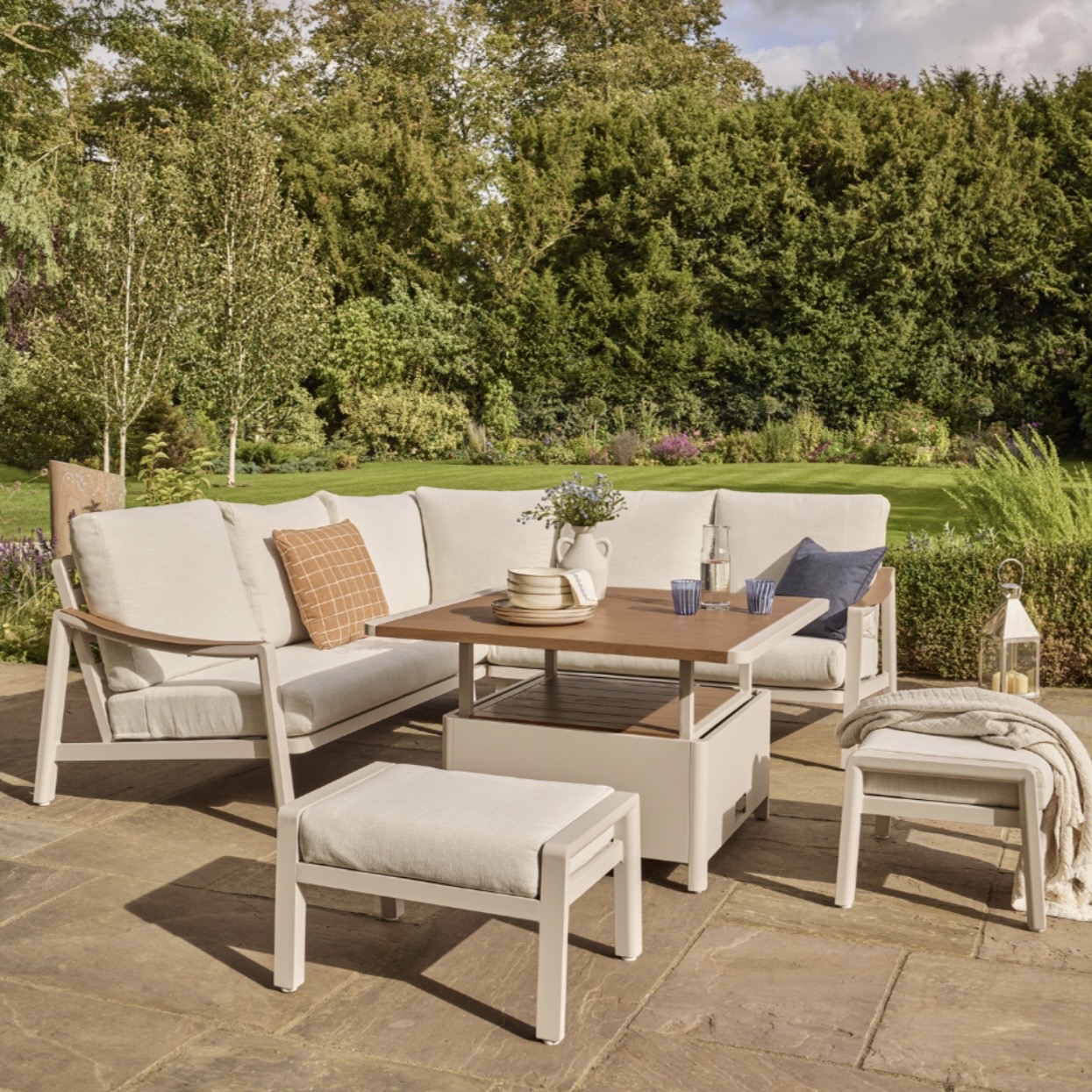 Cream outdoor corner lounge set with stools and a central table on a sunny terrace