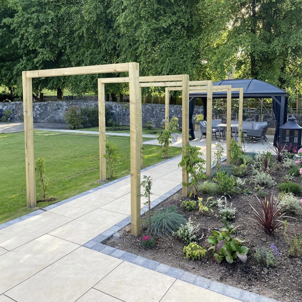 Stone garden edging along a paved pathway with wooden pergola walkway and planted border
