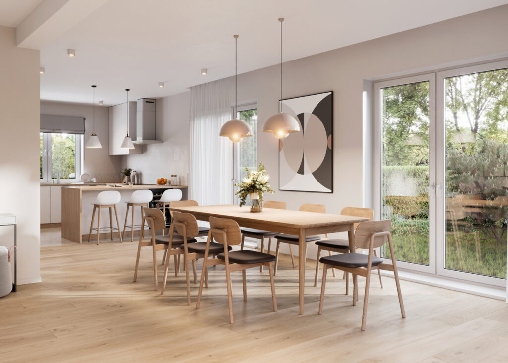 Open plan kitchen dining room with a large wooden dining table, pendant lights, pale cabinetry and garden doors
