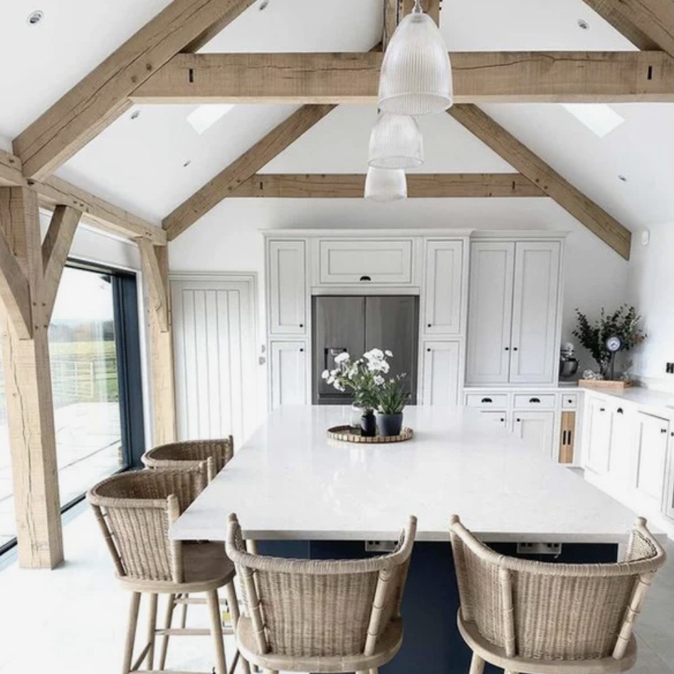 Kitchen dining room ideas with prismatic pendant lighting above a large island in a pale timber-beamed kitchen diner