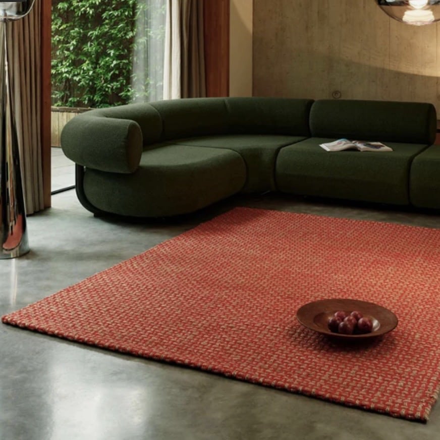 Orange living room with woven burnt orange rug and dark green sofa in a modern interior