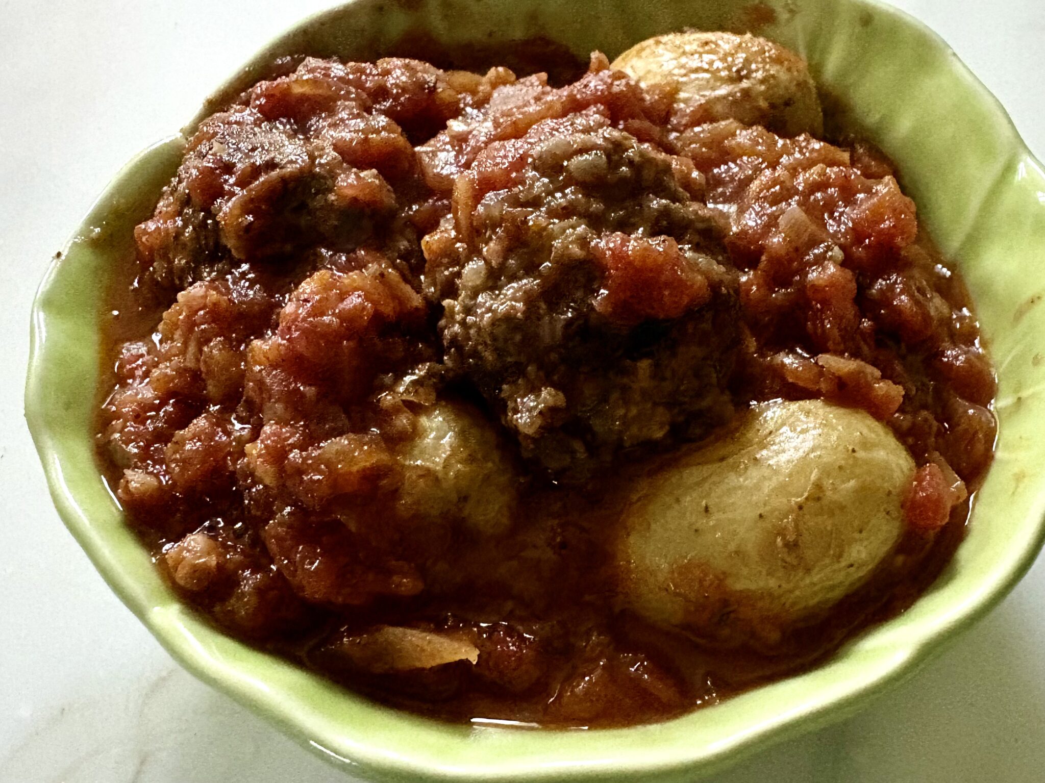 Venison meatballs in rich tomato sauce served with roasted baby potatoes in a green bowl