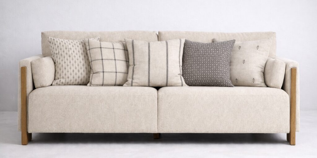 Beige sofa styled with black and beige cushions in checks, stripes and subtle small-scale patterns against a soft grey background