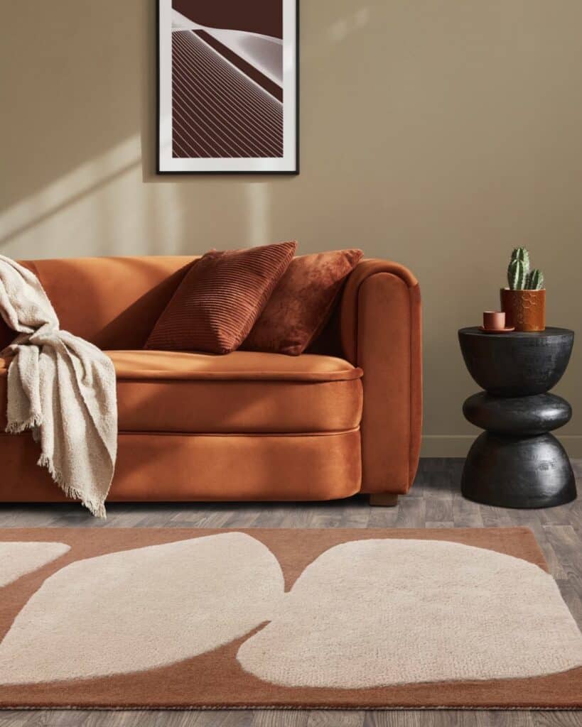 Orange living room with a burnt orange velvet sofa, rust cushions and an orange and cream abstract wool rug