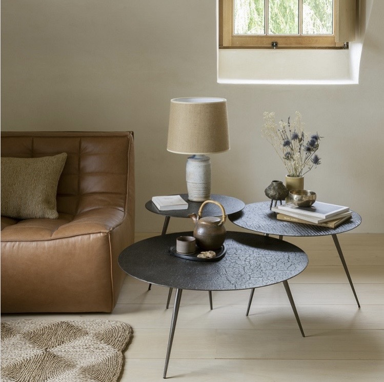 Layered coffee table decor ideas with nested black coffee tables, books, ceramics, and a lamp beside a tan leather sofa in a calm neutral living room.