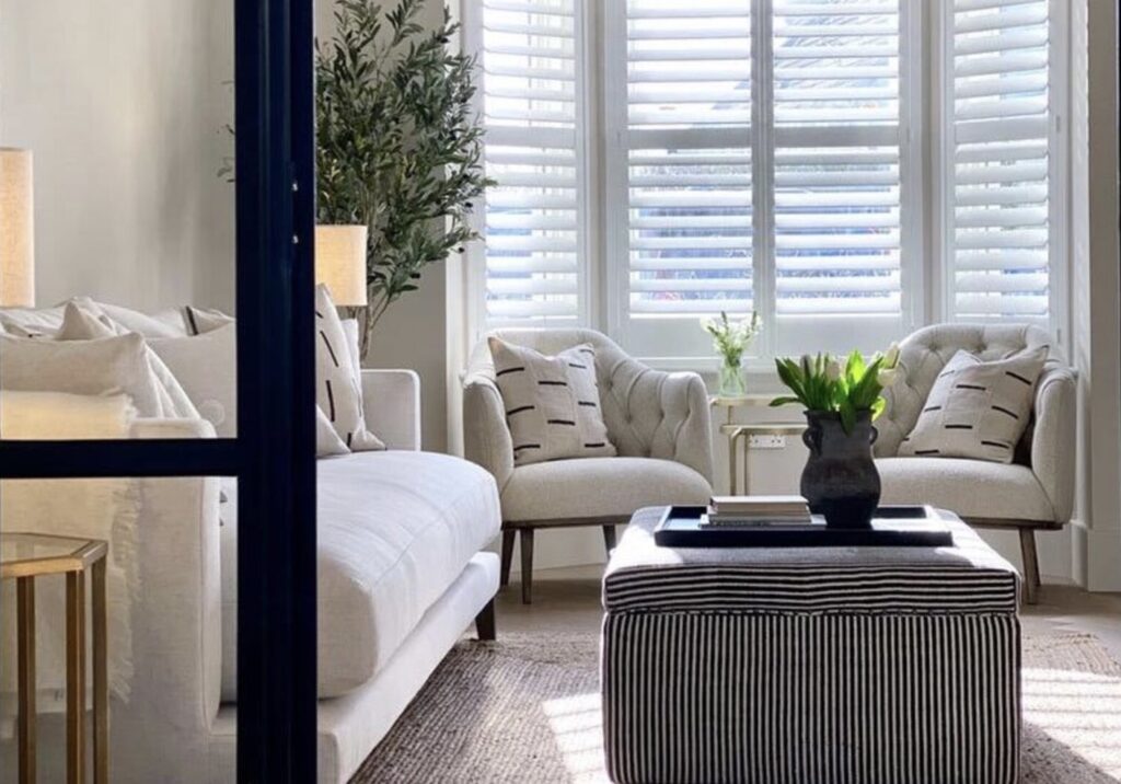 Wooden Black Ottoman Tray on a striped storage ottoman in a bright living room with beige and black cushions, showing practical coffee table styling.