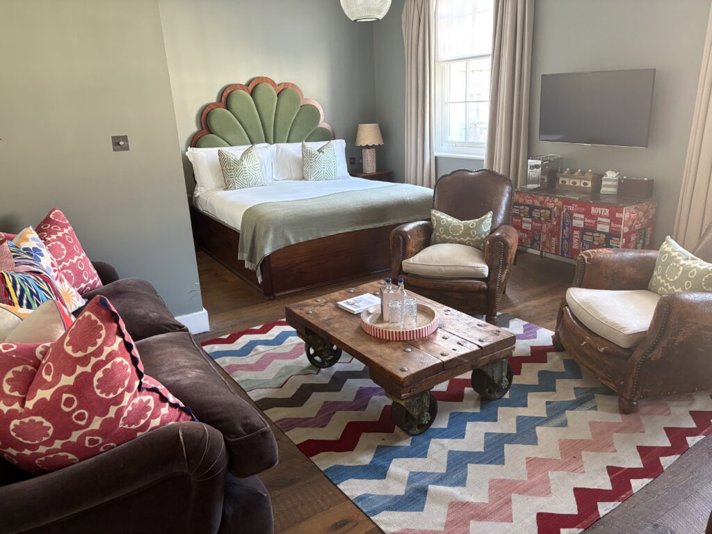 Eclectic style in the Club Suite at Artists Residence London — fan headboard, leather club chairs, factory trolley coffee table and bold cushions