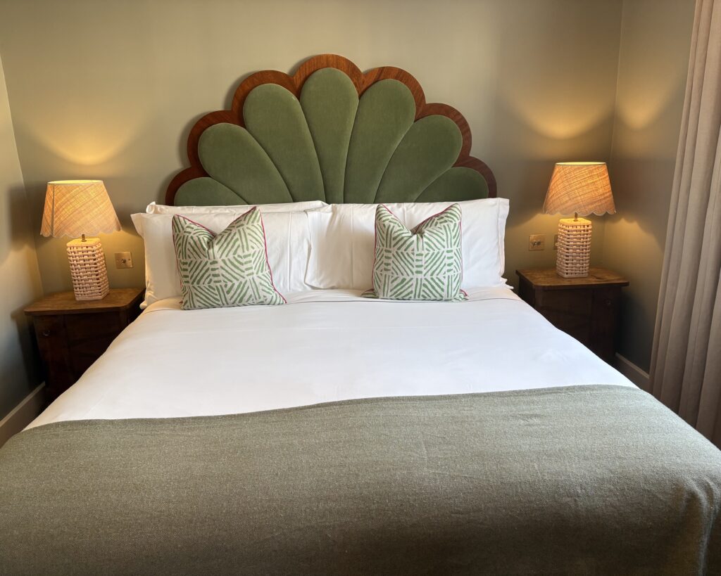 Eclectic bedroom with green velvet fan headboard, rattan lamps and patterned cushions — Artists Residence London Club Suite