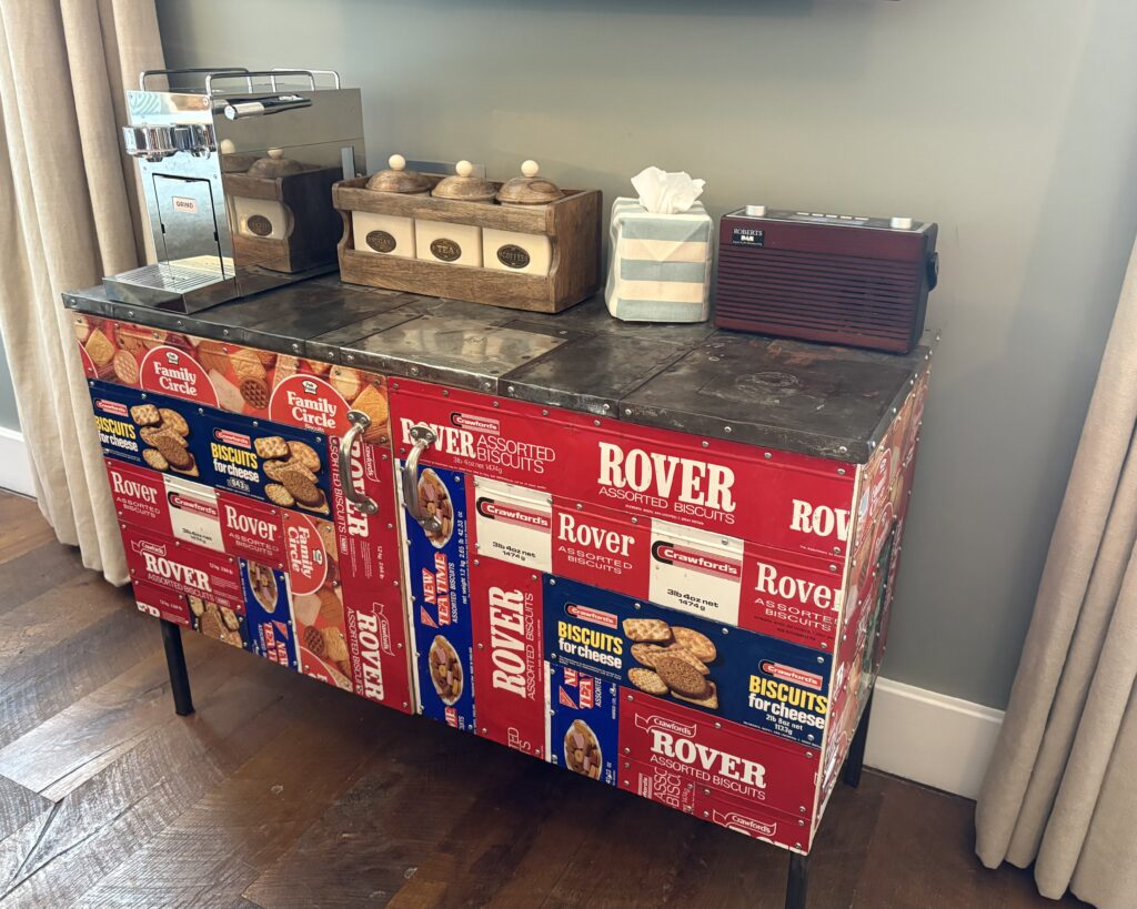Upcycled sideboard covered in vintage Crawford's biscuit tin panels with coffee station — eclectic home decor at Artists Residence London
