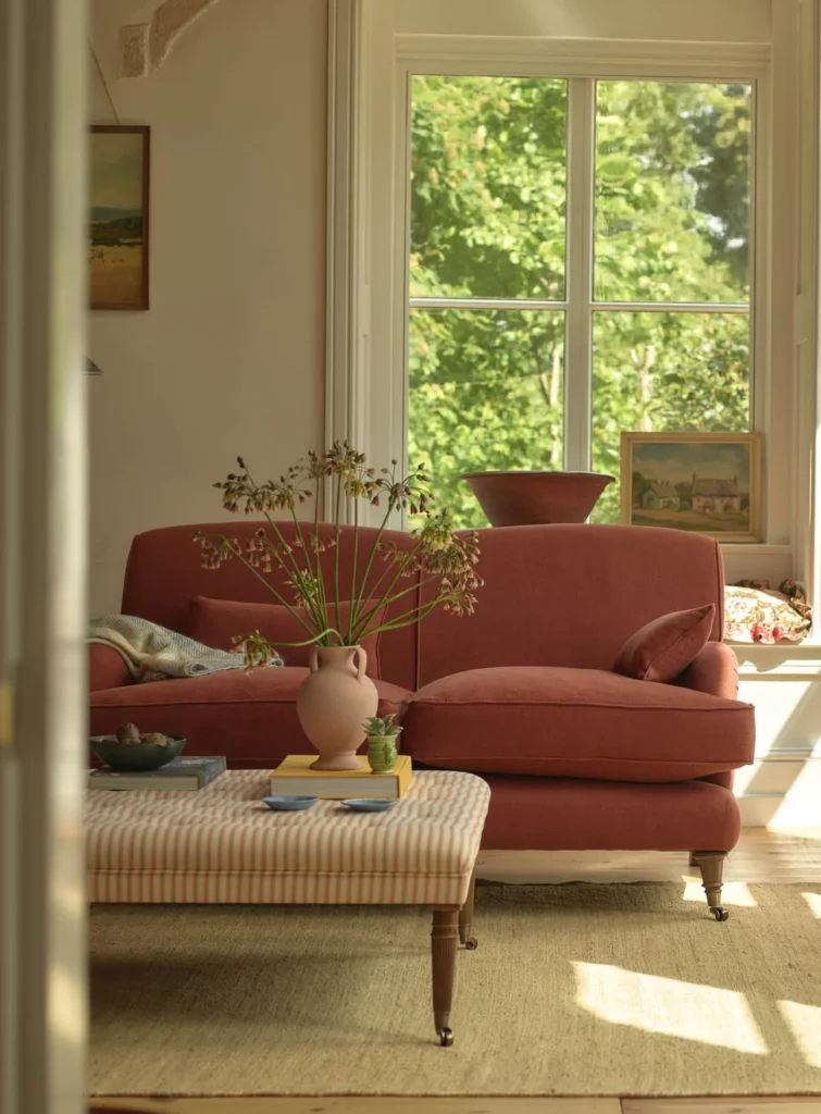 rust linen sofa in orange living room with brass castors allium stems and landscape paintings