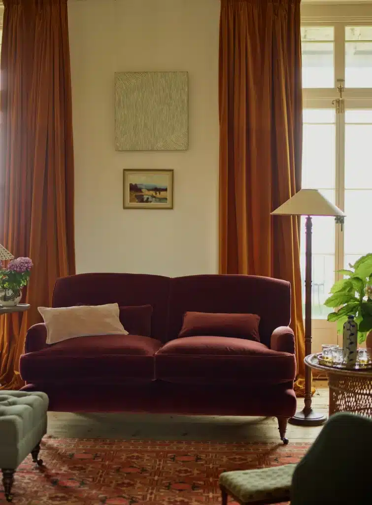 rustic burnt orange living room with rust velvet sofa floor length curtains kilim rug and landscape painting