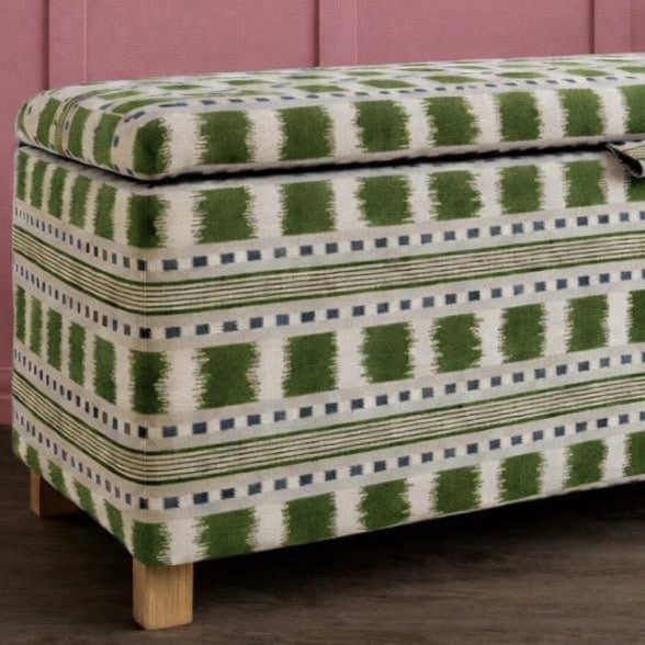Green patterned upholstered ottoman with wooden legs to complete the pink and green bedroom