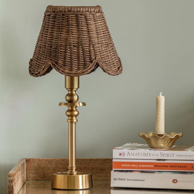 Small rattan scalloped lampshade on a brass lamp base in a pink and green bedroom