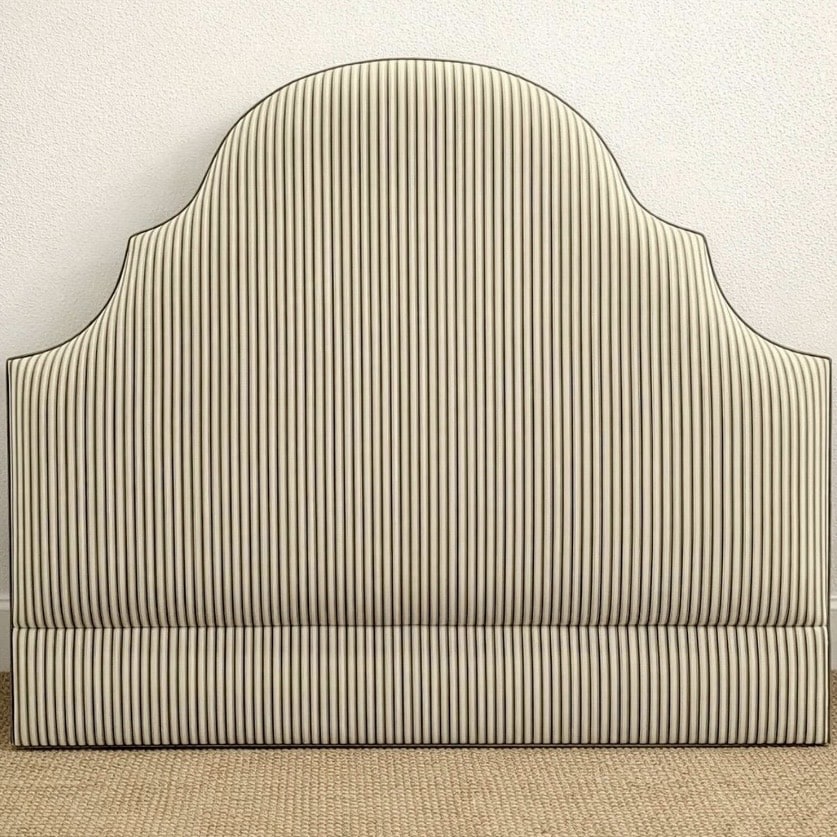 Ticking stripe upholstered headboard in a scalloped shape to ground the pink and green bedroom