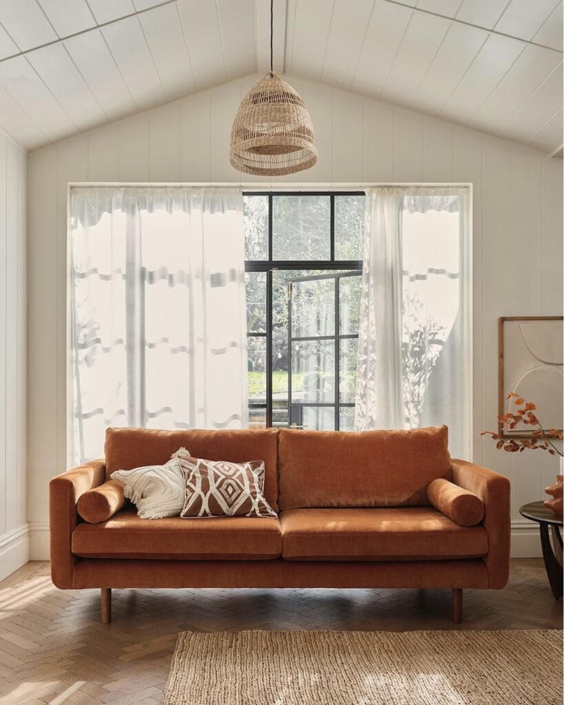 Burnt orange velvet sofa against walls painted in Farrow & Ball Pigeon, with blush pink cushions and a Berber-style rug