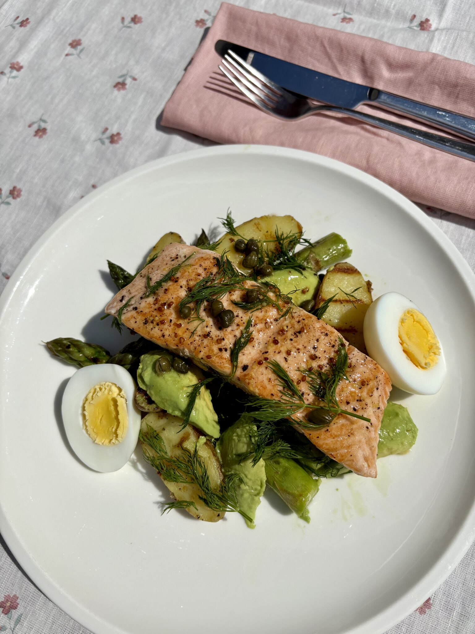 Asparagus and salmon salad with Jersey Royals, avocado, boiled egg, capers and dill on a white plate
