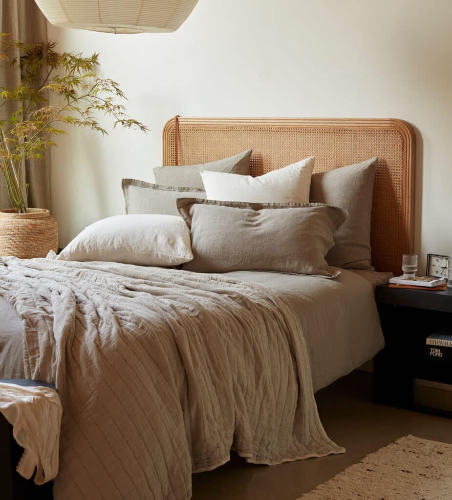 Beige bedroom with layered natural linen bedding in oatmeal and stone, a crinkled linen quilt and a cane headboard