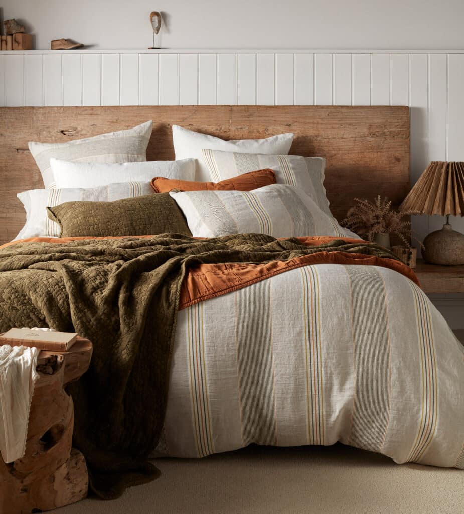 Beige bedroom with Sophie Stripe linen bedding, olive and burnt orange quilts and a reclaimed timber headboard