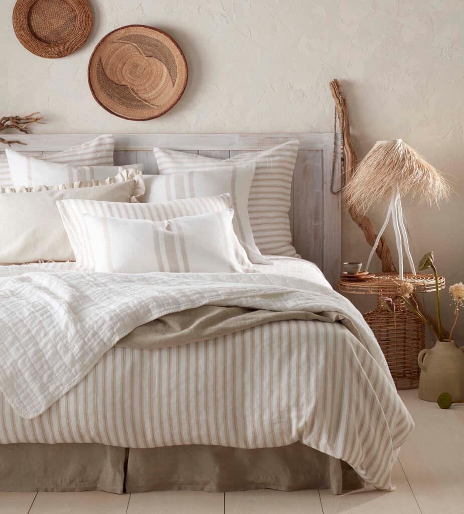 Beige bedroom with French ticking stripe cotton linen bedding, woven wall plates and a raffia table lamp