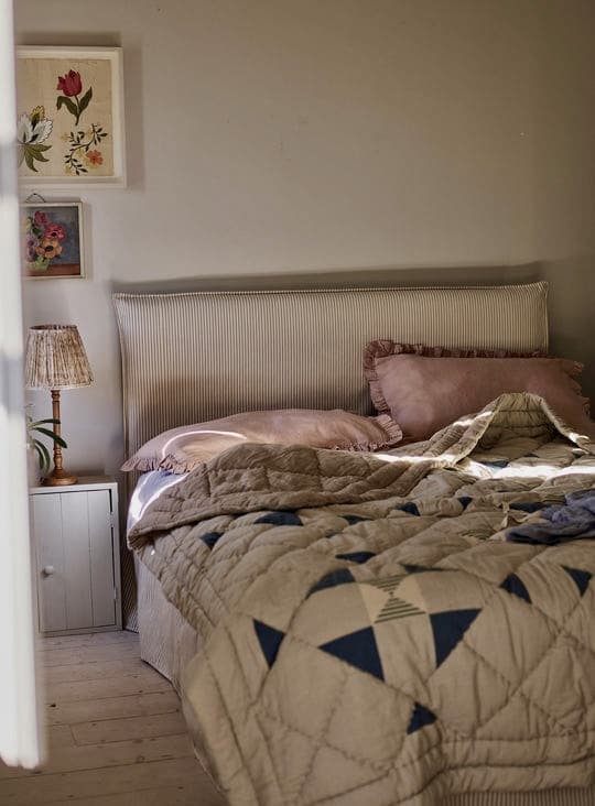 Blue and beige bedroom with Lillie cotton patchwork quilt in dusky blue, blush ruffled pillowcases and a ticking-stripe headboard
