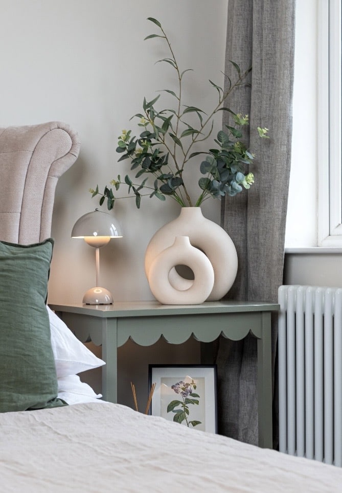 scalloped edge bedside table in soft green styled in a cottage bedroom with lamp and ceramics