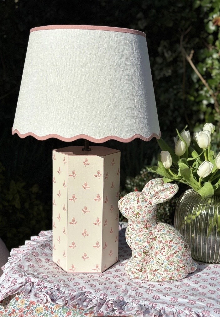 scalloped edge lampshade with pink trim on a floral table setting with ceramic lamp base and spring flowers