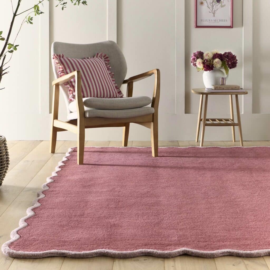 scalloped edge rug in coral and lilac tones styled in a cottage living room with armchair and wooden side table