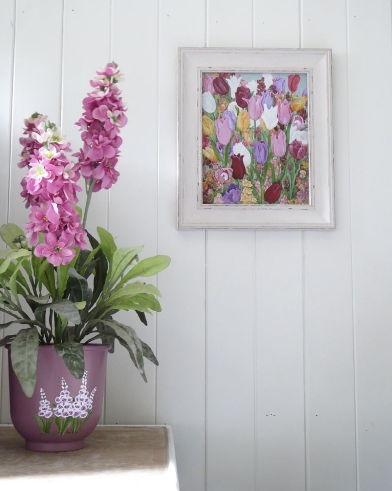 Framed tulip painting above a pink plant pot in soft cottage bedroom decor