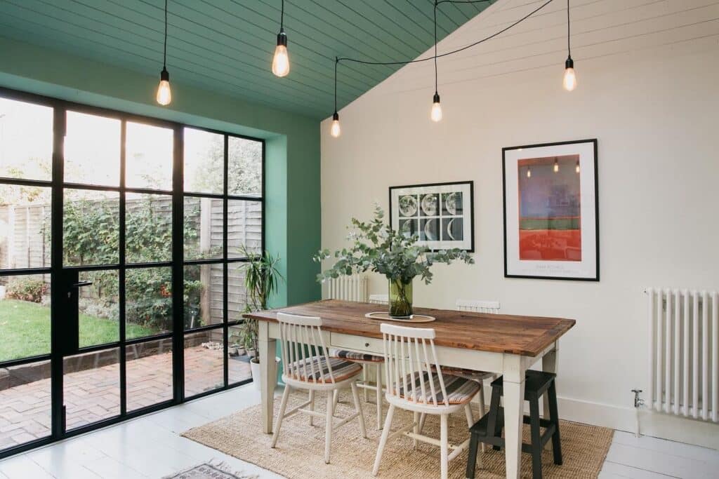 green painted ceiling in Farrow and Ball Arsenic in a kitchen dining room extension with crittall doors and Edison pendants